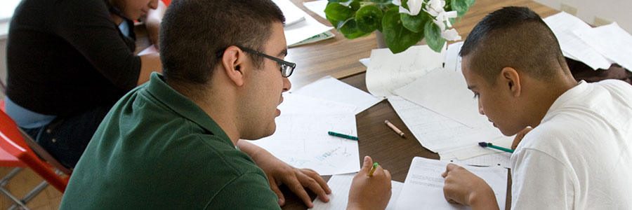 A banner of an image of a young man helping a younger student with his classwork.
