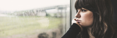 A banner of an image of a young woman staring out the window on a cold, rainy day.