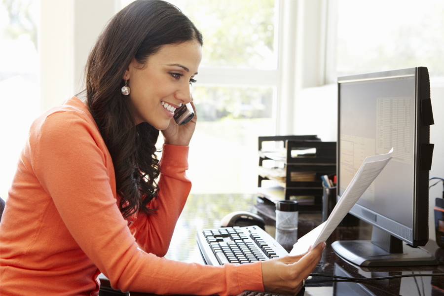 An image of a young woman talking on her phone and looking at her computer screen.