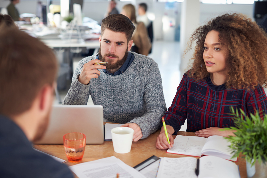 An image of a group of young coworkers sitting with their laptops and having a discussion at work.