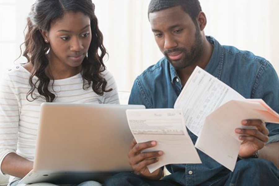 An image of a man and woman holding a laptop and looking at papers.