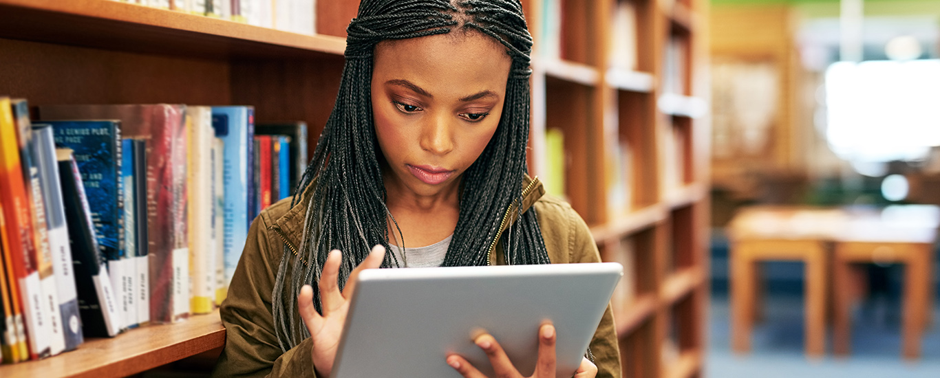 An image of a young woman looking at her tablet computer in the library.