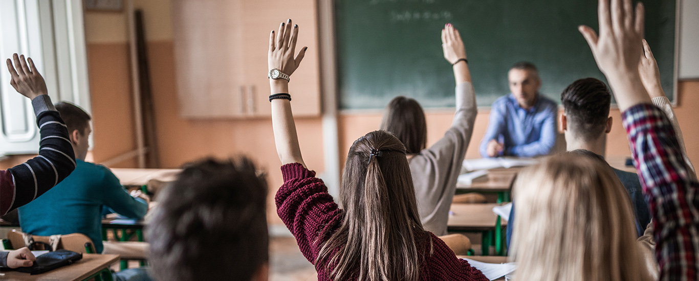 An image of a group of students raising their hands to answer the teacher.