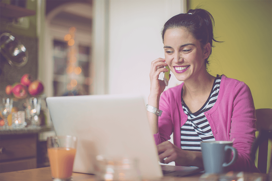 An image of a young woman sitting in front of her laptop and talking on her cellphone.